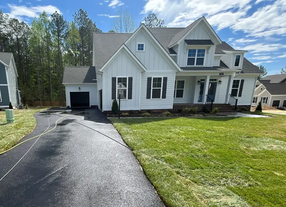 White farmhouse new build with a freshly washed asphalt driveway and a hose line across the lawn