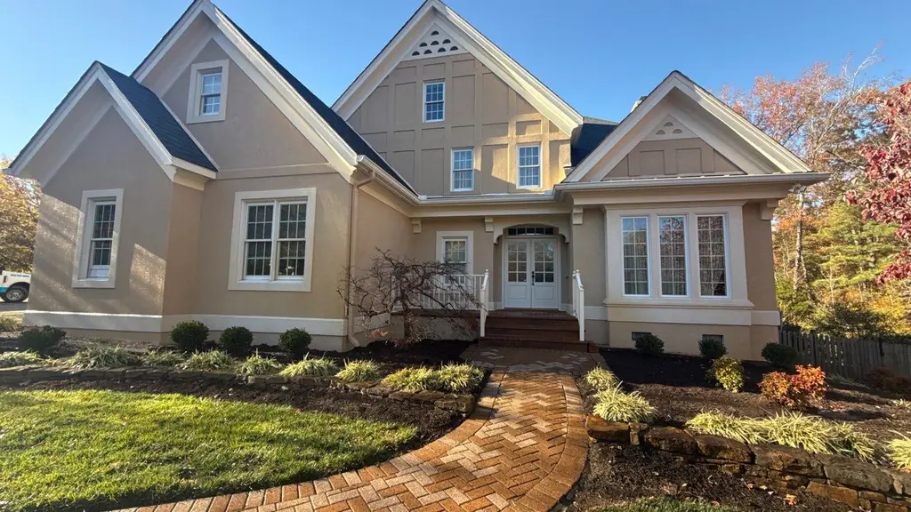Tan home with a brick front walk, porch steps and autumn planting beds