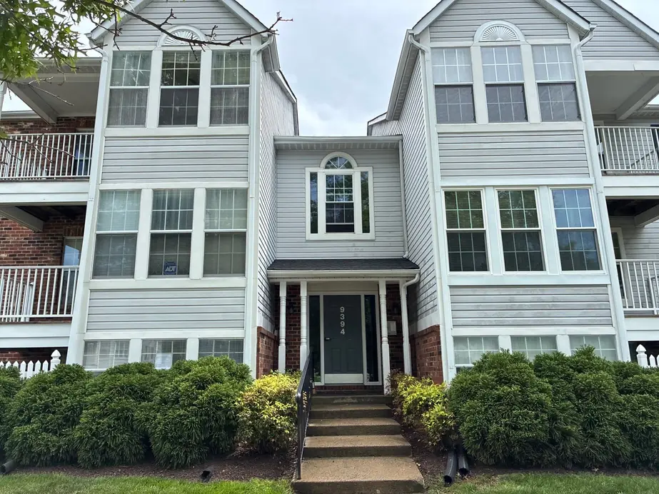 Grey vinyl multi-family entrance with a brick base and clipped shrubs